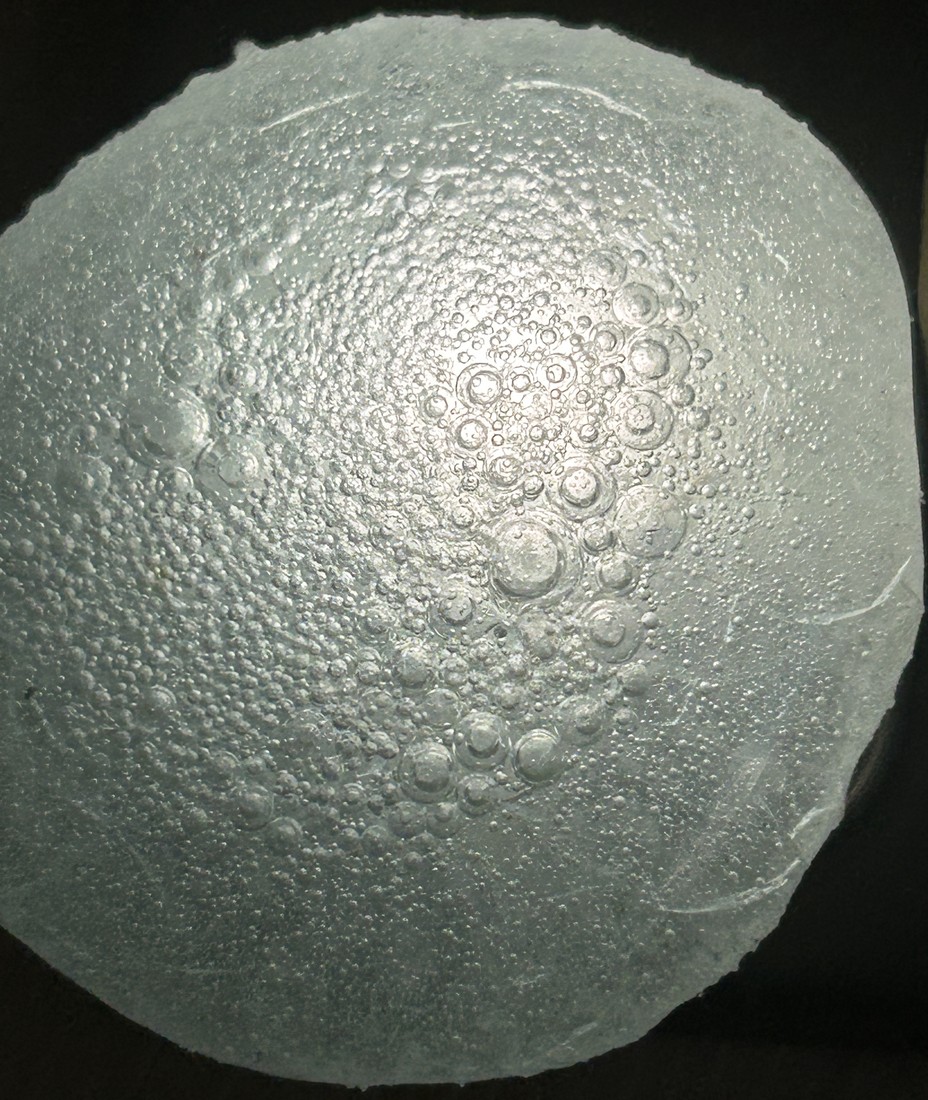 Fused disc of plain glass from the revised firing, lit from behind against black